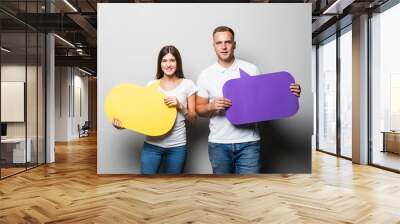 Smiling pretty couple holding blank bubbles speech isolated on gray background Wall mural